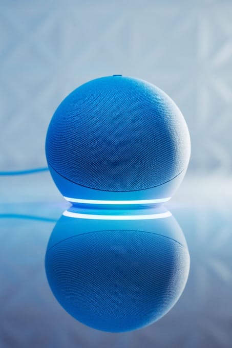 Caixa de som inteligente Amazon echo dot 5 em formato esférico azul com anel luminoso aceso e reflexo na superfície.